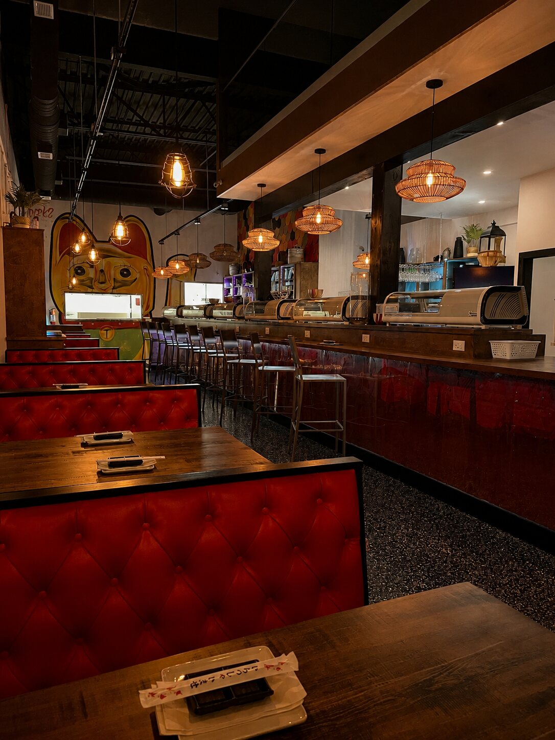 The sushi bar glowing under warm pendant lights, with red booths and a relaxed evening ambiance.