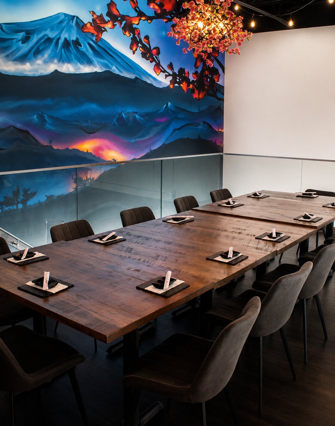 The private mezzanine's Mount Fuji mural — snow-capped peak, blue mountains and a sunset glow with cherry blossoms — above a long communal dining table.