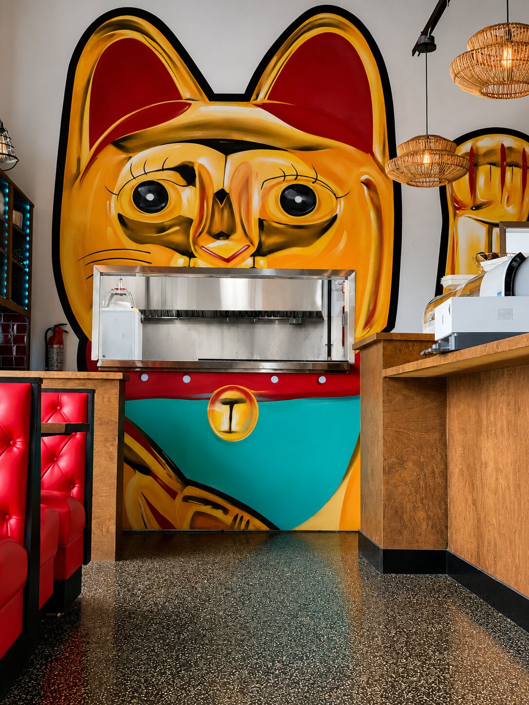 The massive hand-painted golden lucky-cat mural — Kōna's mascot — filling the wall behind the host stand, with red booths alongside.