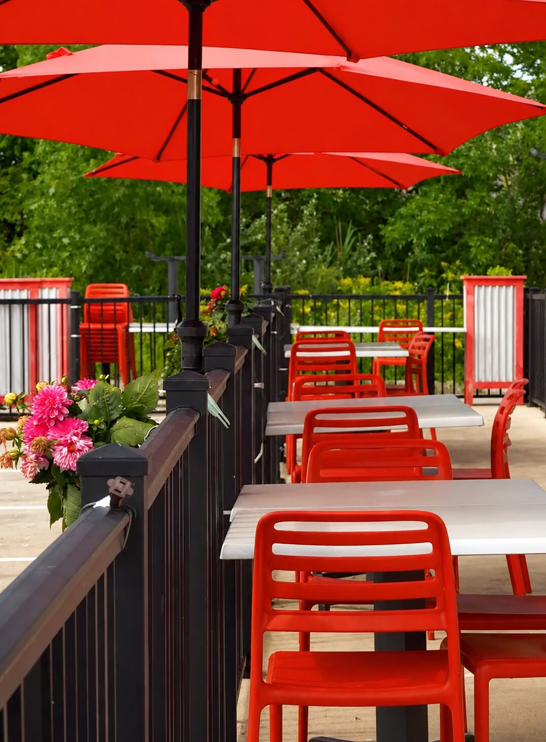 The outdoor patio in summer — red umbrellas and chairs surrounded by flowers and greenery.