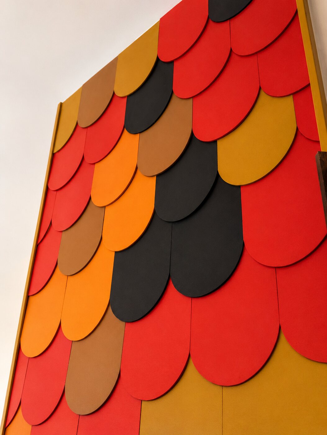 A sculptural fish-scale feature wall of dimensional red, orange, gold and black shingles.