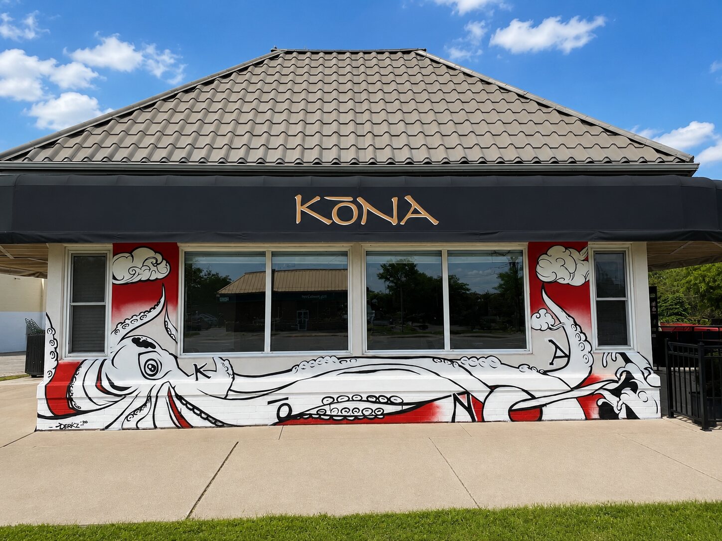 The Kōna LaSalle storefront wrapped in its black-and-white street-art octopus mural on a red backdrop, gold KŌNA signage above, blue sky.