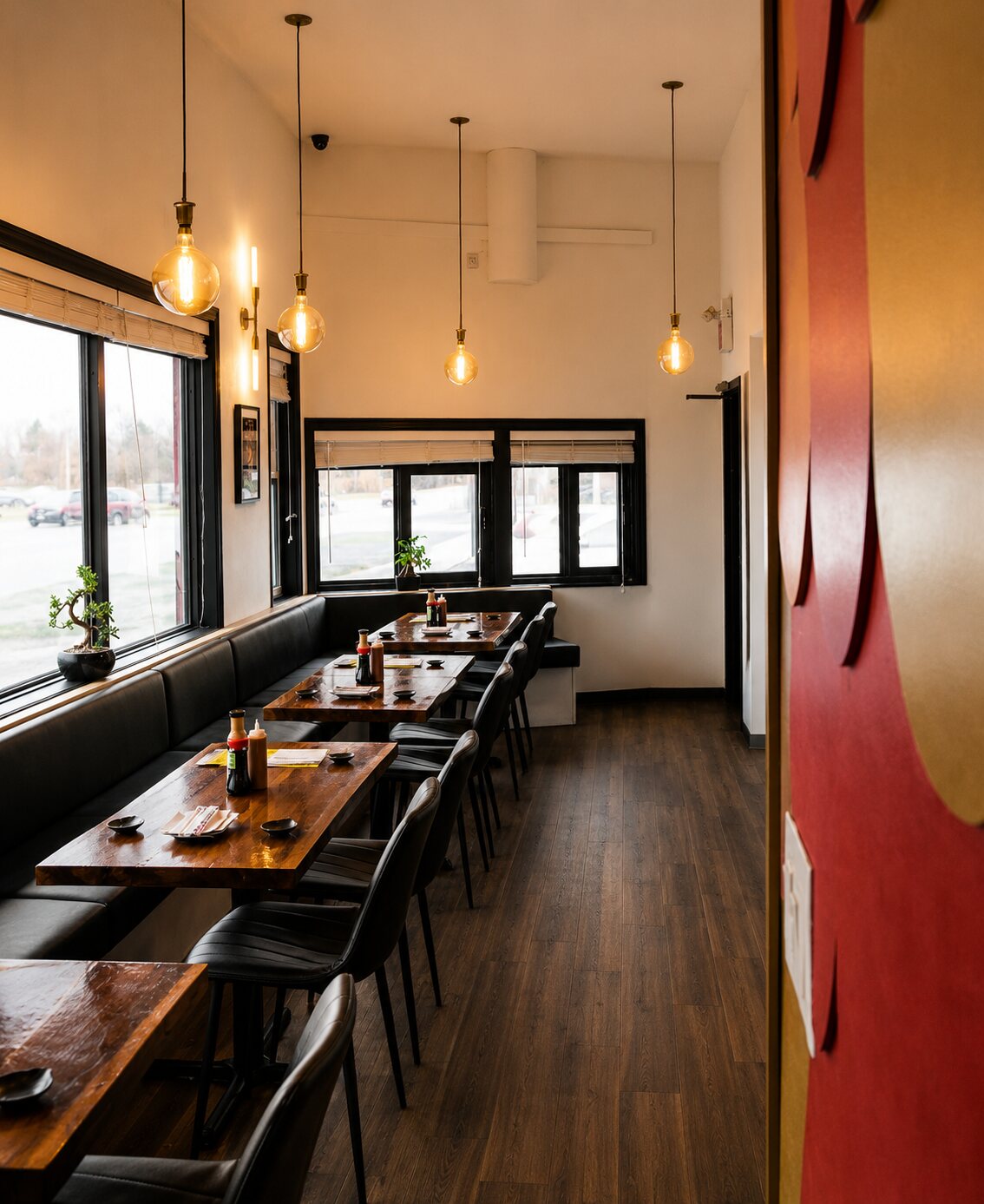 A dining row with a banquette, wood tables, globe pendant lights and a bonsai beside the fish-scale wall.
