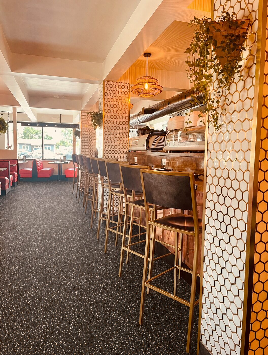 Wide interior — the bar with gold stools, red booths and honeycomb columns glowing under warm light.