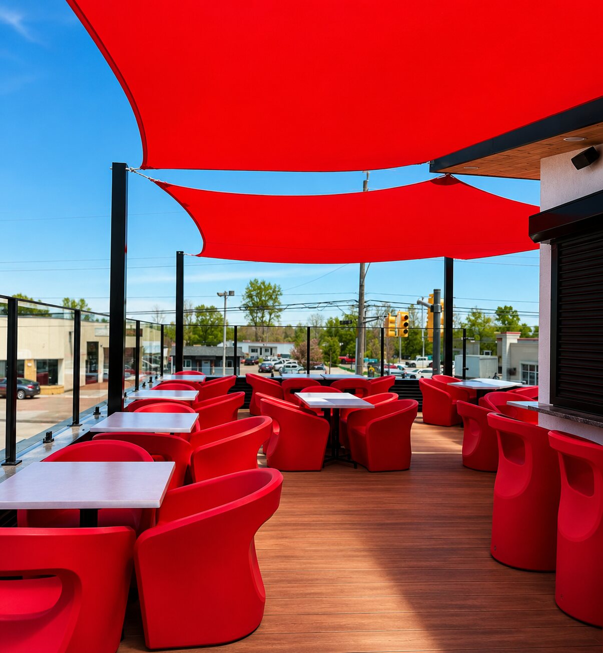 The rooftop patio by day — rows of red lounge chairs and tables on the wood deck under red sail shades and open sky.