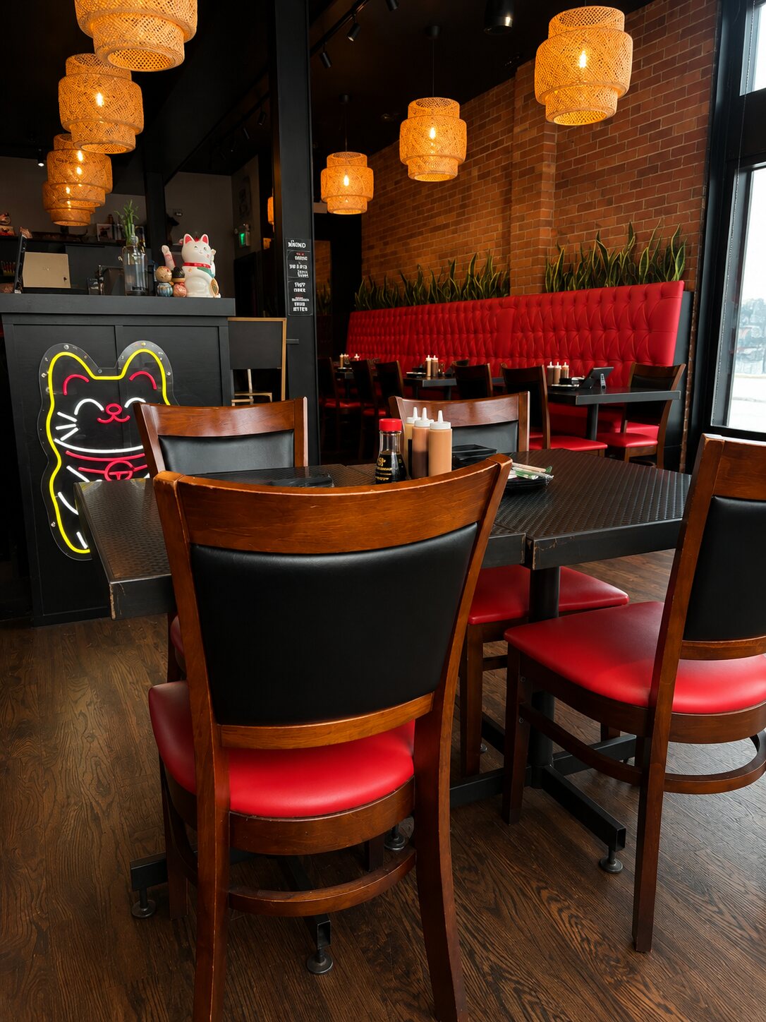 The bar glowing under a neon lucky-cat sign — red banquette along exposed brick, cascading rattan pendants and the sushi counter.