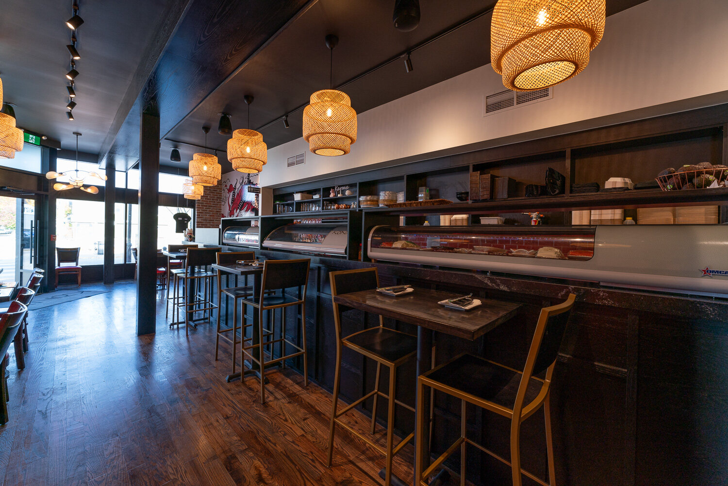 A long red tufted banquette against exposed brick with snake plants, cascading rattan pendants and a sushi display case.