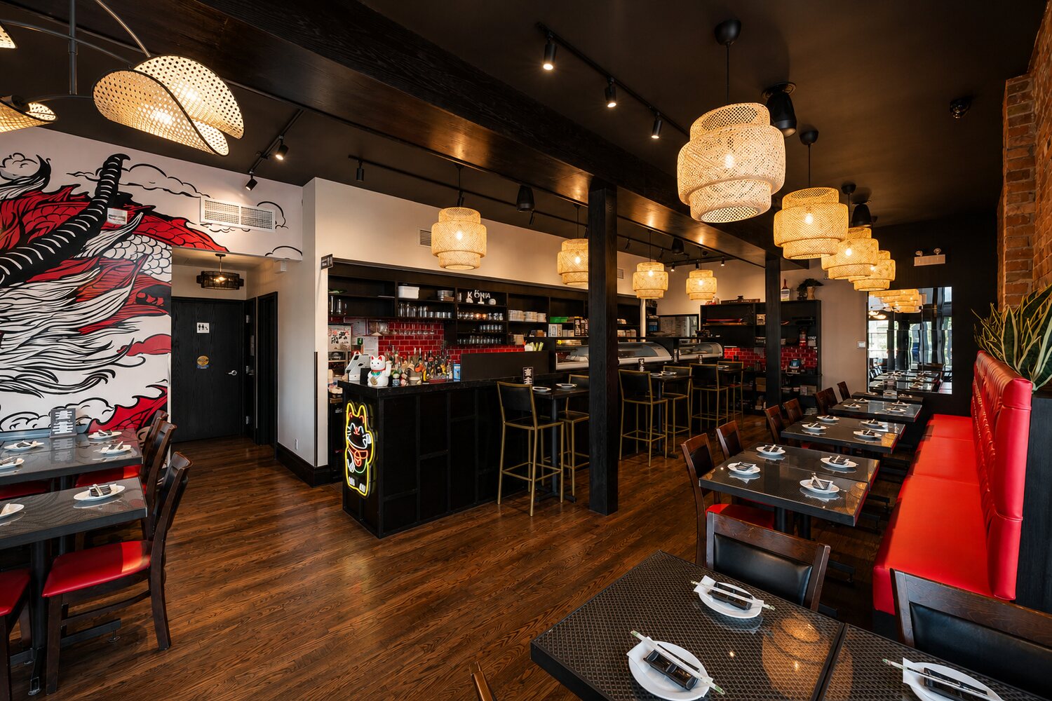 Tables with red chairs beneath the neon lucky-cat sign, warm and lively.